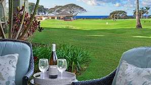 Une chaise en osier, une bouteille de vin et deux verres posés sur une petite table, le tout offrant une vue imprenable sur un magnifique terrain de golf verdoyant et sur l’océan.