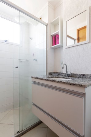 Un baño con cabina de ducha de vidrio, lavabo con encimera de mármol y espejo sobre el lavabo.