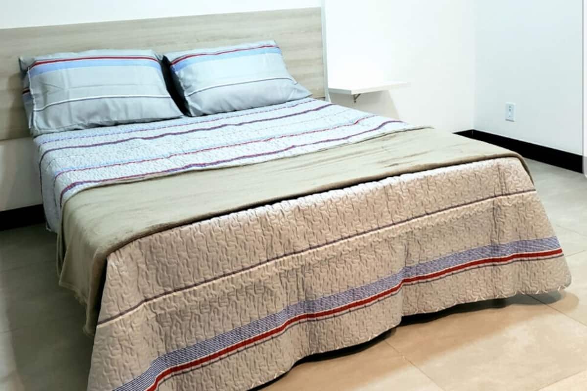 Ein Bett mit gestreifter Bettdecke und zwei Kissen, ein Nachttisch und eine Steckdose.