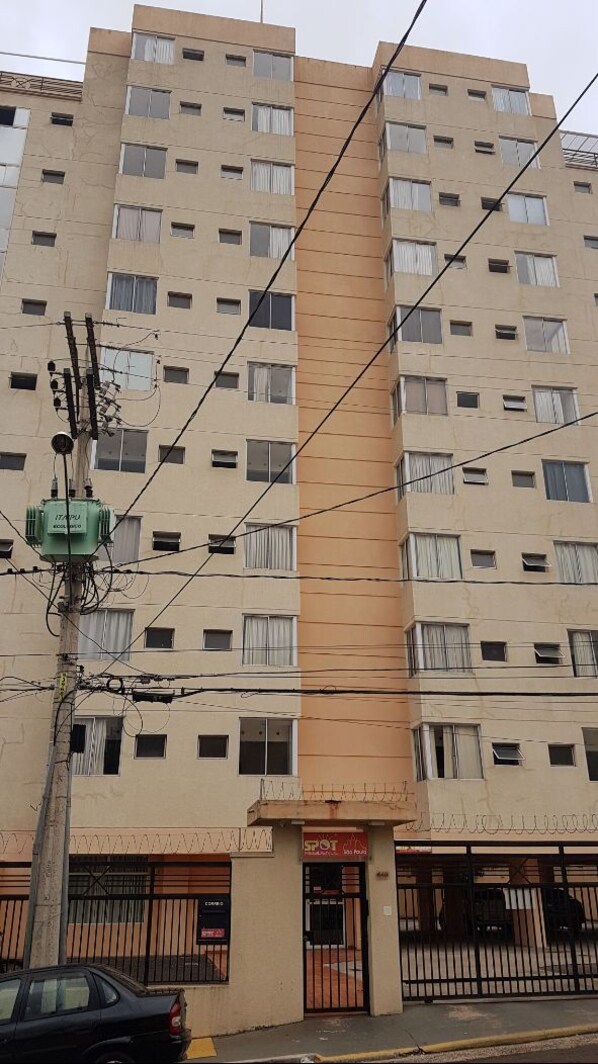 Un edificio de varios pisos con fachada color crema, múltiples ventanas y una tienda visible en la planta baja.