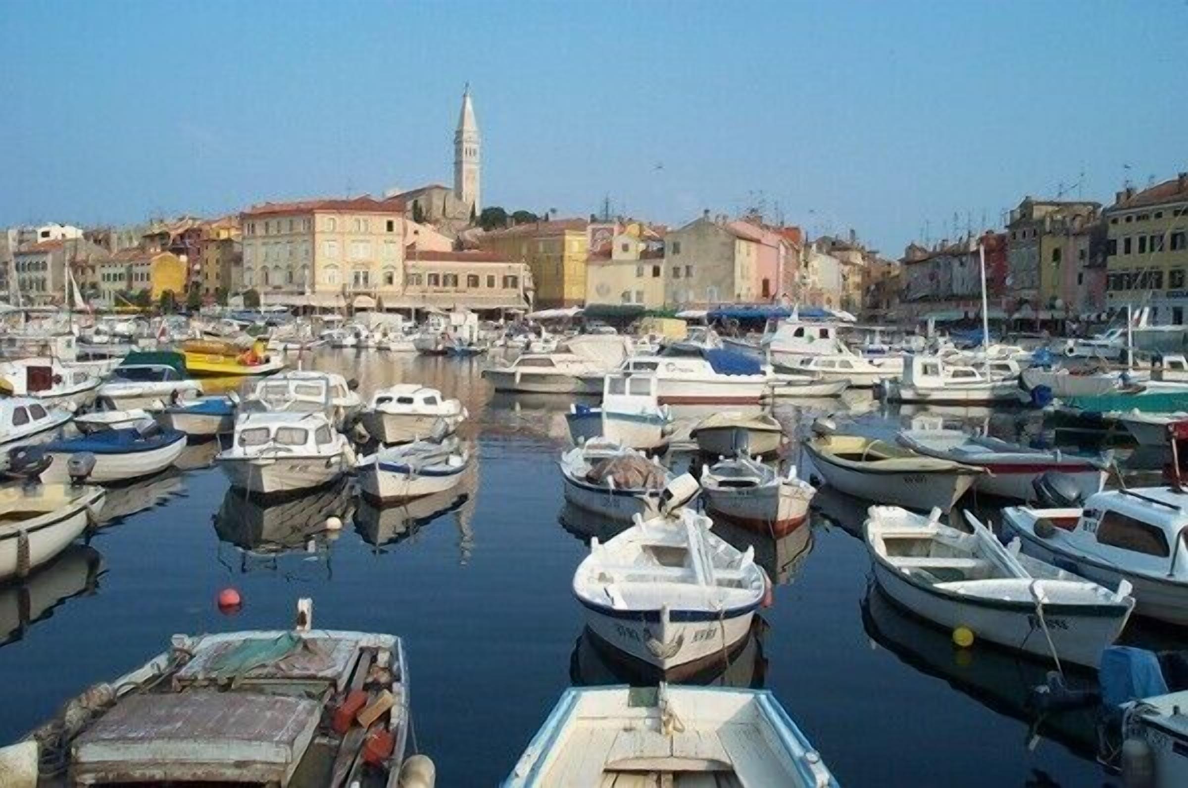 A marina filled with various boats, surrounded by historic buildings and a prominent tower.
