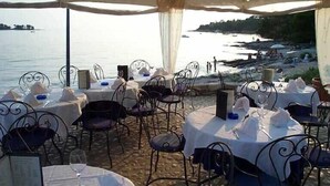 Area pranzo all'aperto con tavoli imbanditi per due, con vista su uno specchio d'acqua.