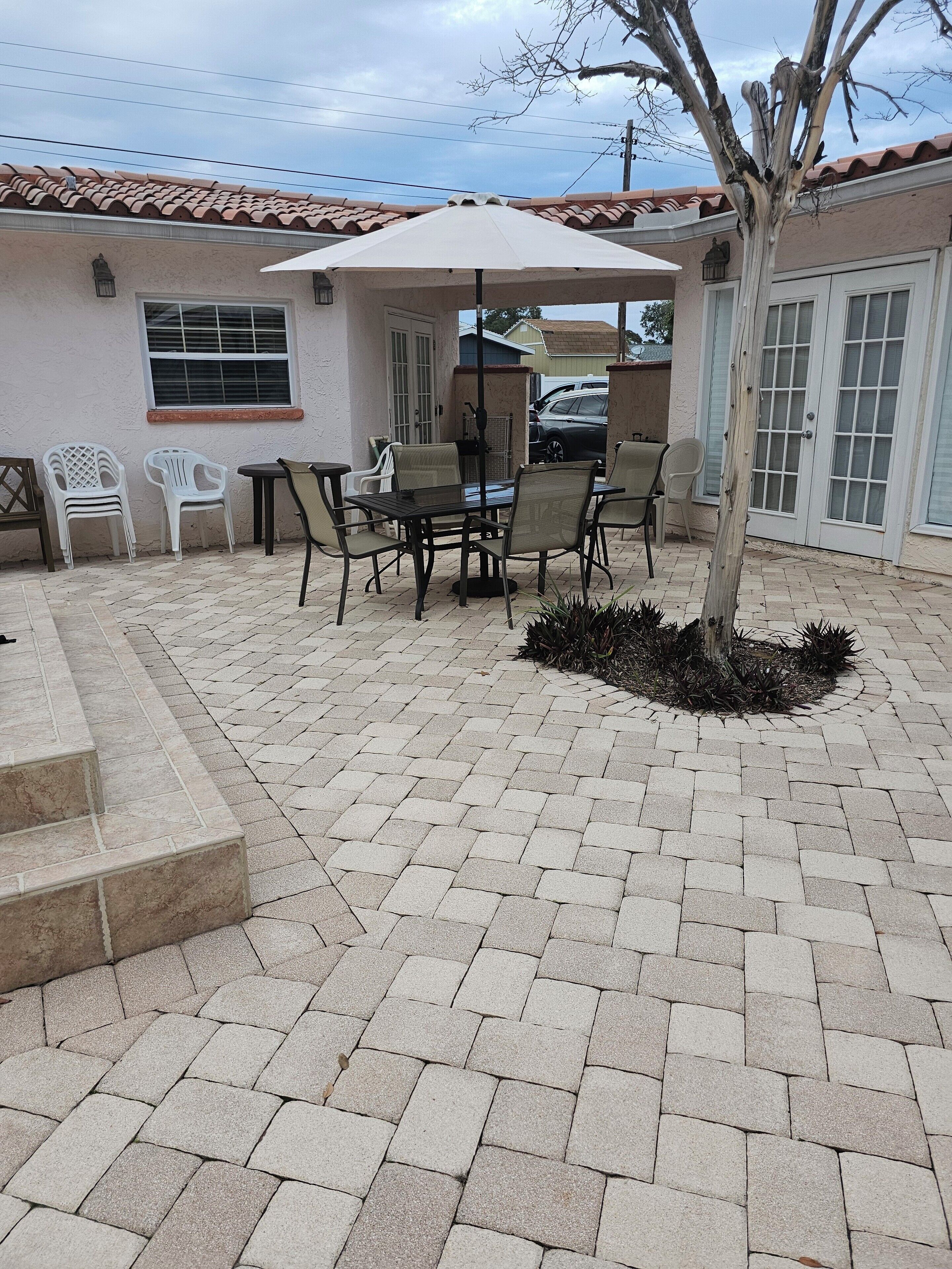 A patio with a table and chairs, a small tree, and a brick floor.