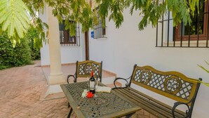 A patio with two wooden benches and a table, a bottle of wine, and a glass.
