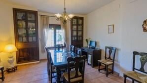 A dining area with a glass-top table, wooden chairs, a chandelier, and a cabinet with glass doors.