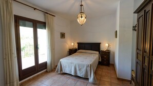 A bedroom with a bed, bedside tables, a chandelier, and a sliding glass door leading to an outdoor area.