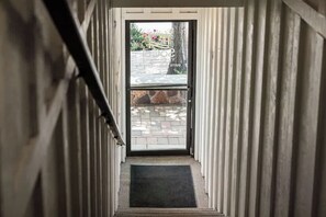 Passadís estret que condueix a una porta, amb un mur de pedra i un jardí petit visible a través d'ella.