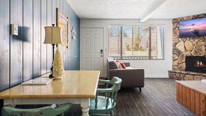 A cozy living room with a fireplace, a dining area, and a seating area with a couch and chairs. - Teddy Bear, Perfect Location in the Village (Big Bear Lake)