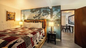 A bedroom with a large bed, a wooden headboard, a nightstand with a lamp, and a painting of a forest on the wall. - Polar Bear, Perfect Location, hot tub (Big Bear Lake)