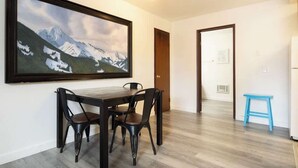 A dining area with a wooden table and chairs, a large framed picture on the wall, and a blue stool. - Polar Bear, Perfect Location, hot tub (Big Bear Lake)