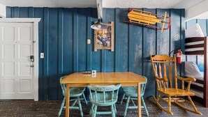 Ein Zimmer mit Holztisch und -stühlen, einem Holzschaukelstuhl, einem gerahmten Bild an der Wand und einem Schild, das anzeigt, dass es sich um eine 'Ski Lodge' handelt.