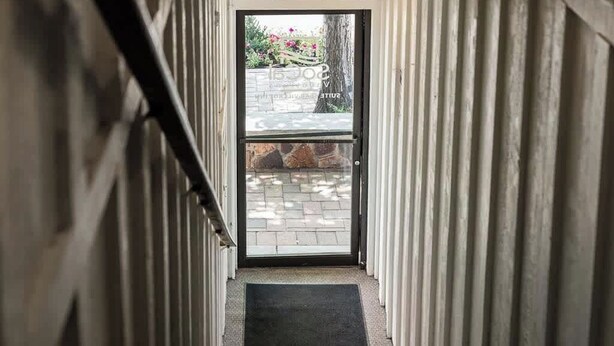A narrow hallway with a door leading to an outdoor area with a stone wall and a tree. - Grizzly Bear, Perfect Location in the Village (Big Bear Lake)