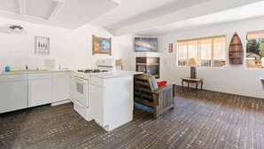 A compact kitchen with a stove, oven, and white cabinetry. There is a small seating area with a bench and a table. - Grizzly Bear, Perfect Location in the Village (Big Bear Lake)
