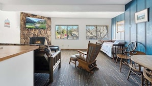 A cozy living room with a stone wall, fireplace, and large windows. - American Black Bear. Perfect Location (Big Bear Lake)
