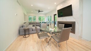 Een moderne woonkamer met een glazen eettafel, een grijze bank en een open haard.
