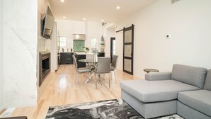 Een moderne woonkamer met een grijze modulaire bank, een eethoek met een glazen tafel en stoelen, en een keuken op de achtergrond.