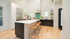 Een moderne keuken met een groot eiland, barkrukken en een roestvrijstalen koelkast.