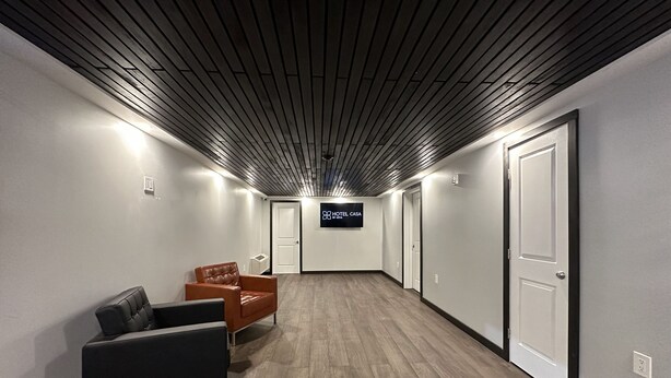 A hallway with a wooden floor, a black leather sofa, an orange leather chair, and a sign for 'HOTEL CASA'.