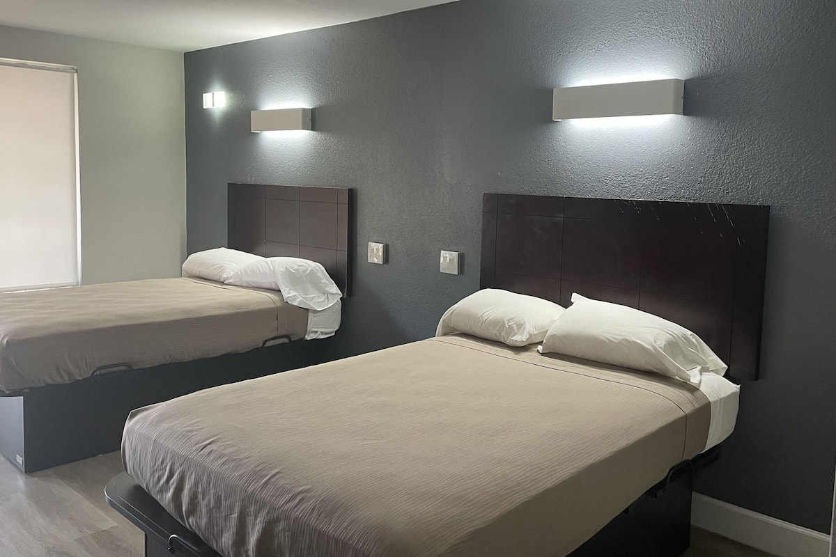 Hotellihuone, jossa on kaksi sänkyä, ja jokaisessa sängyssä on pääty ja valkoiset vuodevaatteet.