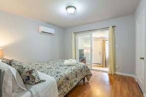 A bedroom with a bed, a window, an air conditioning unit, and a door leading to another room. - Marbella Lane Duplex Redwood City (Redwood City)
