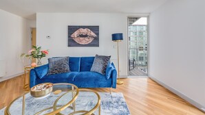 A modern living room with a blue sofa, a glass coffee table, and a painting of lips on the wall.