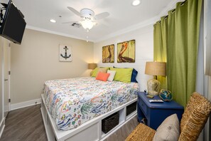 Une chambre à coucher comprenant un lit, un ventilateur de plafond, des œuvres d’art, une lampe et un téléviseur.