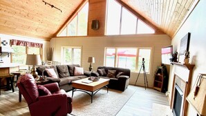 Un salón amplio con techo alto, vigas de madera, chimenea y un ventanal que proporciona luz natural.