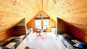 Un dormitorio acogedor en el ático, con techo inclinado, dos camas de madera, una mesita y un ventanal.