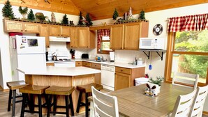 Una cocina con armarios de madera, una isla central y un comedor con sillas blancas.