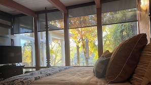 A bedroom with a large bed, a television, and a view of autumn trees through large windows. - Home on Hot Springs beautiful Lake Hamilton. TWO MASTER SUITES!!  (Hot Springs)