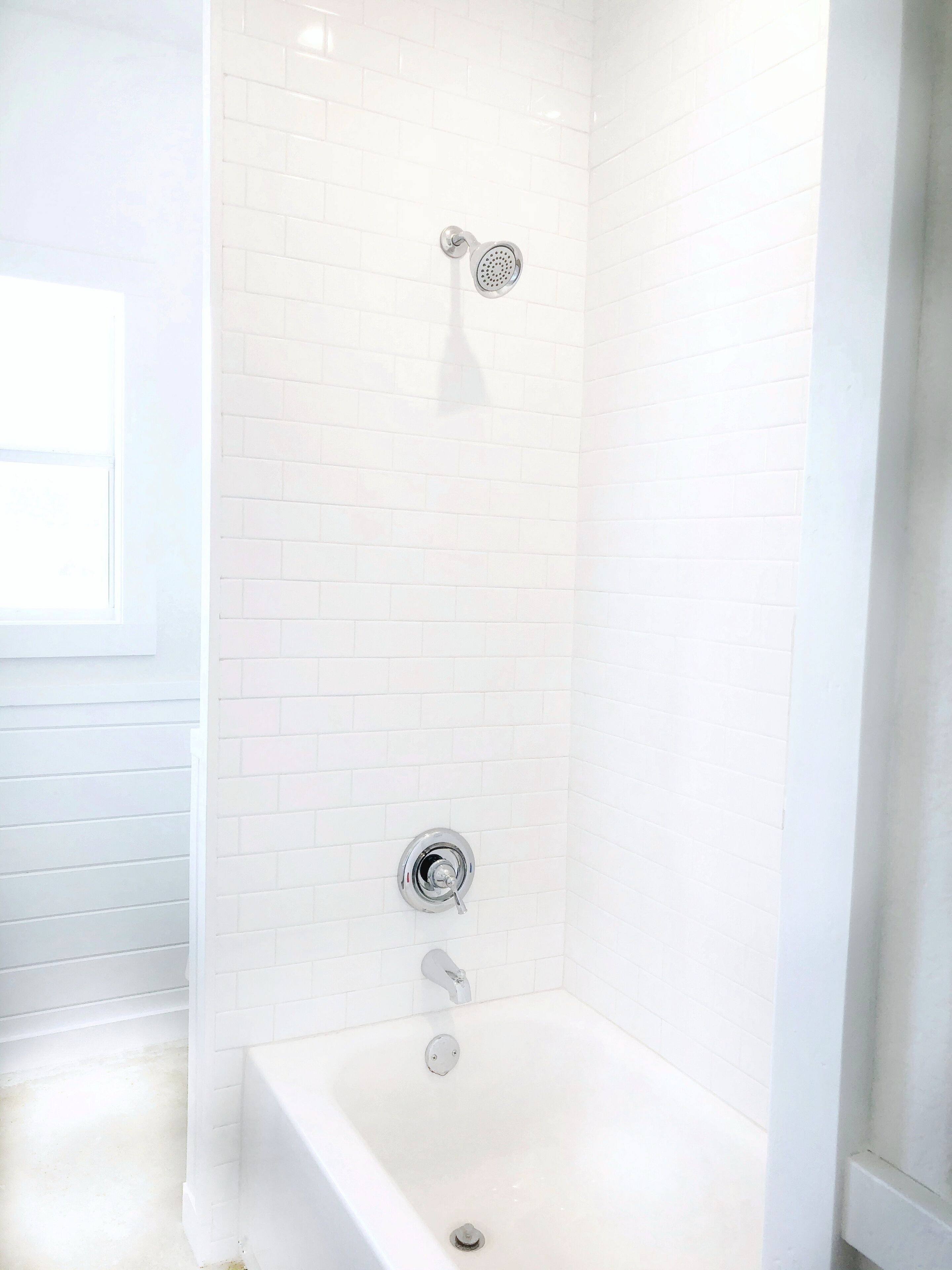 A modern bathroom with white tiled walls, a freestanding bathtub, and a showerhead.