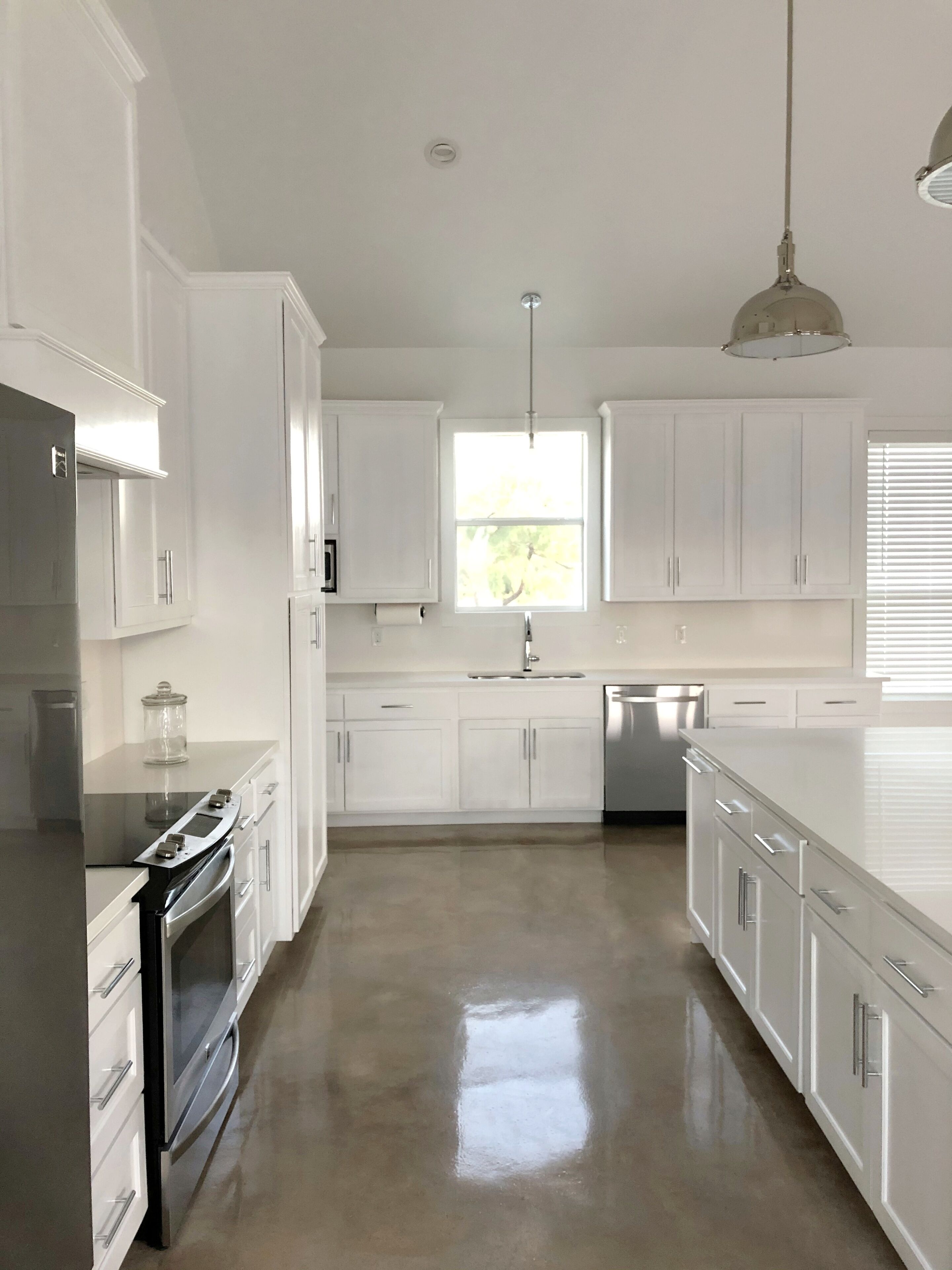 A modern kitchen with white cabinetry, stainless steel appliances, and a large window providing natural light.