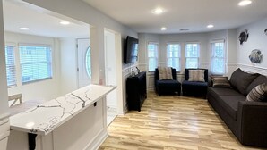 Ein geräumiges Wohnzimmer mit Holzboden, einem dunkelgrauen Sofa und einer weißen Marmorarbeitsplatte.