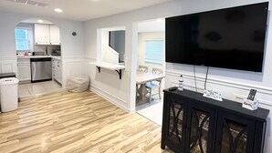 Ein modernes Wohnzimmer mit einem großen Flachbildfernseher an der Wand, einem schwarzen Konsolentisch und einem Holzboden im Fischgrätmuster.