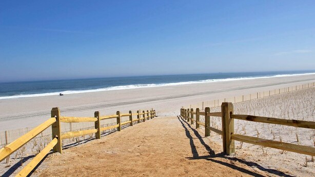 A sandy beach with a wooden fence leading to the ocean.