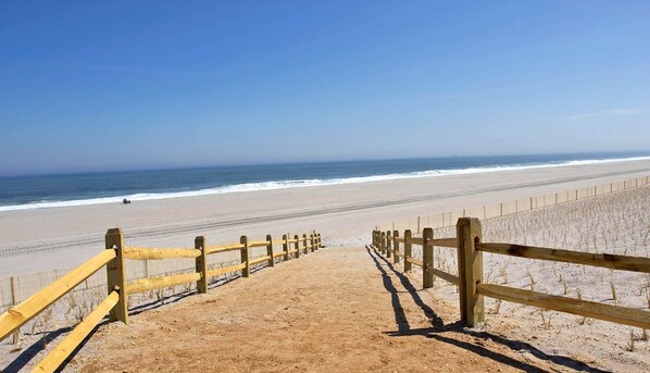Une plage de sable bordée d’une clôture en bois qui mène à l’océan.