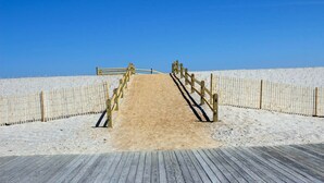 A wooden boardwalk leading to a sandy beach area with a wooden fence on both sides.
