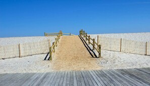 Une promenade en bois mène à une plage de sable, et de chaque côté, une clôture en bois borde le chemin.