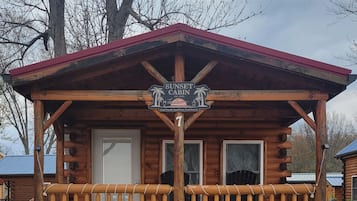 Eine Holzhütte mit rotem Dach, einer Veranda mit Geländern und einem Schild, auf dem 'Sunset Cabin' steht.