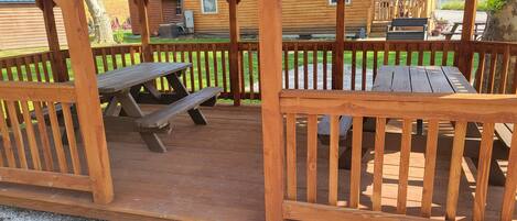 Un patio in legno con tavoli da picnic e una recinzione di legno.