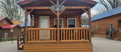 A wooden cabin with a porch, a sign indicating it is the Sunset Cabin, and a gravel ground.