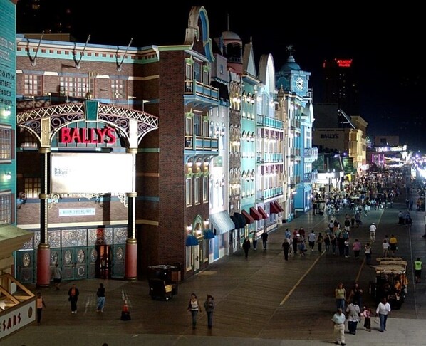A brightly lit casino area with a prominent 'BALLY'S' sign, a wide pedestrian walkway, and various shops along the sides.