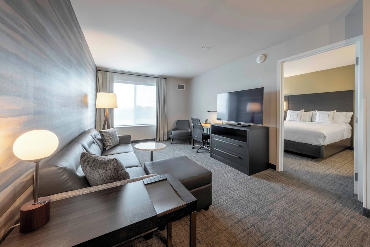 A modern hotel room with a sofa, a desk, a television, and a bed.
