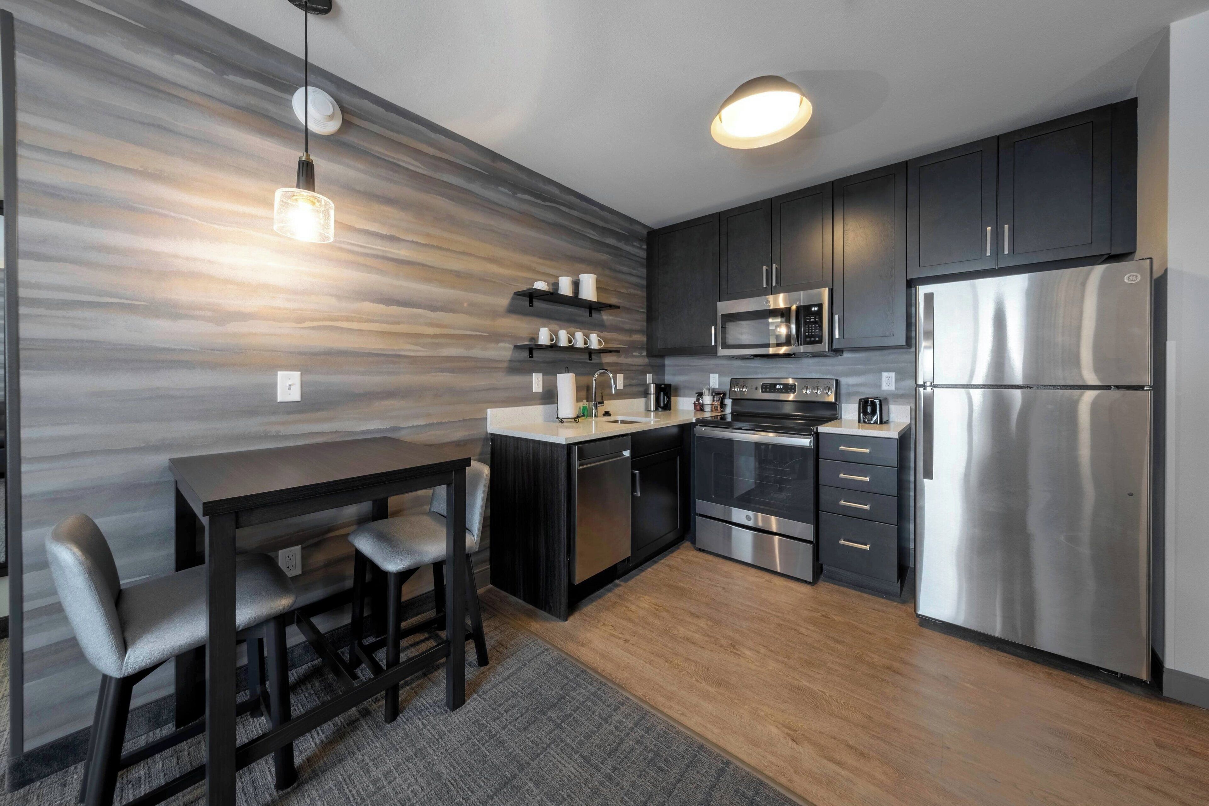 A modern kitchen with dark cabinets, stainless steel appliances, and a dining area with a table and chairs.