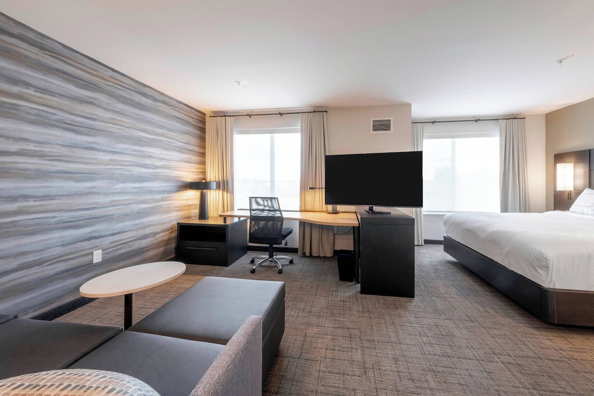 A hotel room with a large bed, a desk with a computer, a chair, a small round table, and a sofa.