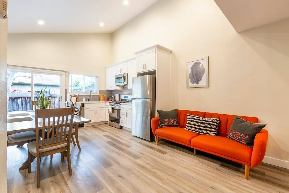 Una cocina moderna con armarios blancos, electrodomésticos de acero inoxidable y una zona de comedor con mobiliario de madera.