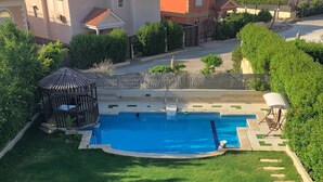 En swimmingpool omgiven av en välskött gräsmatta, med en pergola och en slang utlagd för användning.