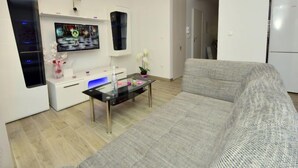 Ein modernes Wohnzimmer mit grauem Sofa, einem Glastisch, einem flachbildfernseher an der Wand und einer weißen Kommode mit blauer Beleuchtung.