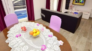 Ein modernes Wohnzimmer mit einem runden Esstisch, violetten Stühlen, einer Couch und einem Fernseher an der Wand.