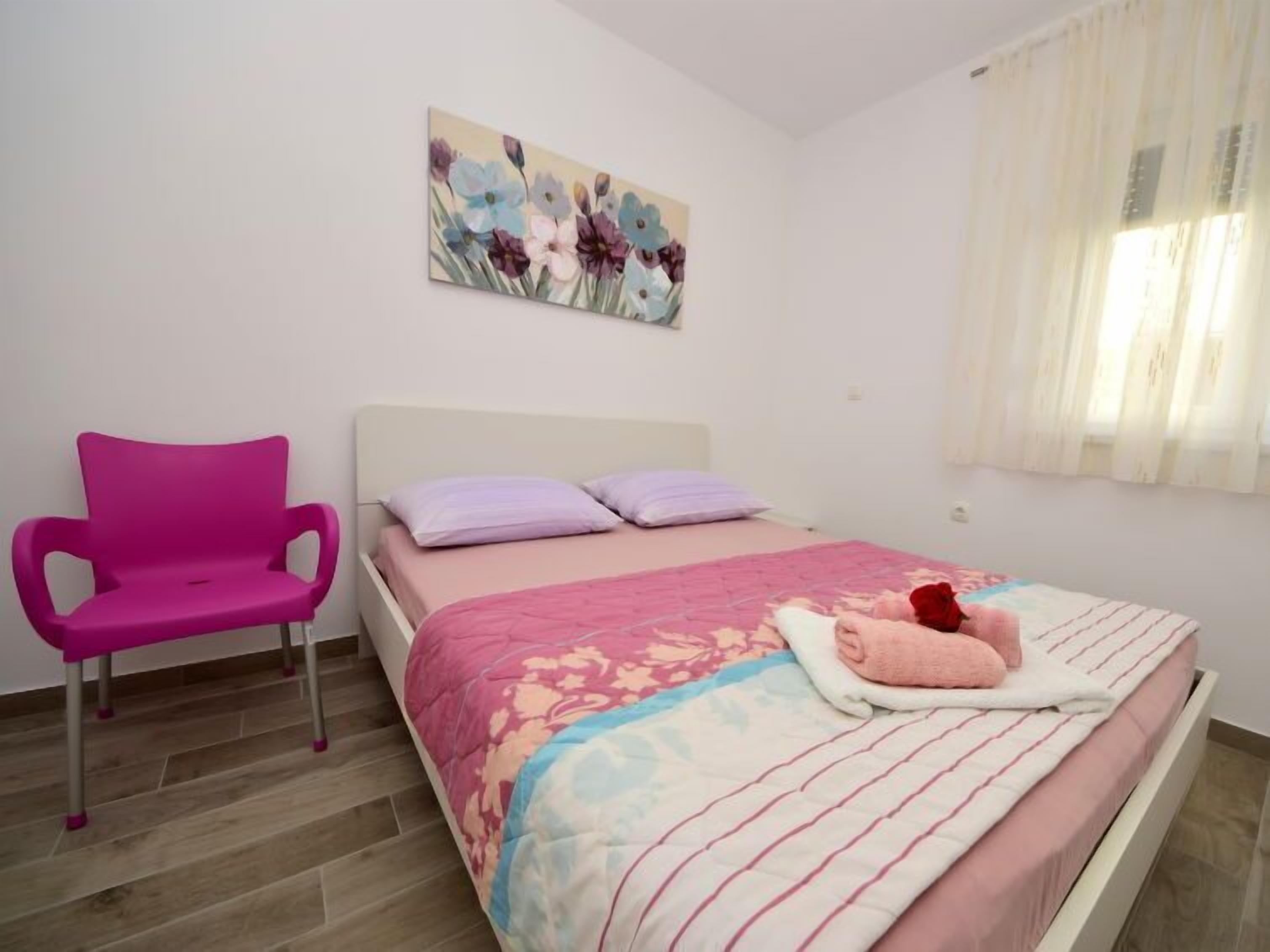 Ein Schlafzimmer mit einem Bett, einem rosa Sessel und einem Bild an der Wand.